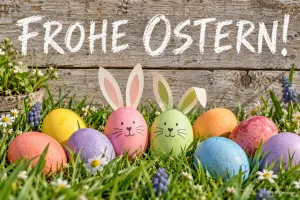Reihe bunter Ostereier, zwei davon mit Hasenohren, Text: FROHE OSTERN!