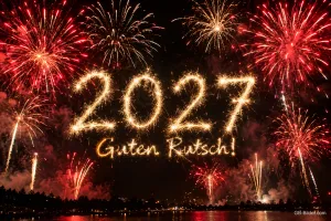 Rotes Feuerwerk mit Jahreszahl über dem Wasser, Text: 2027 – Guten Rutsch!